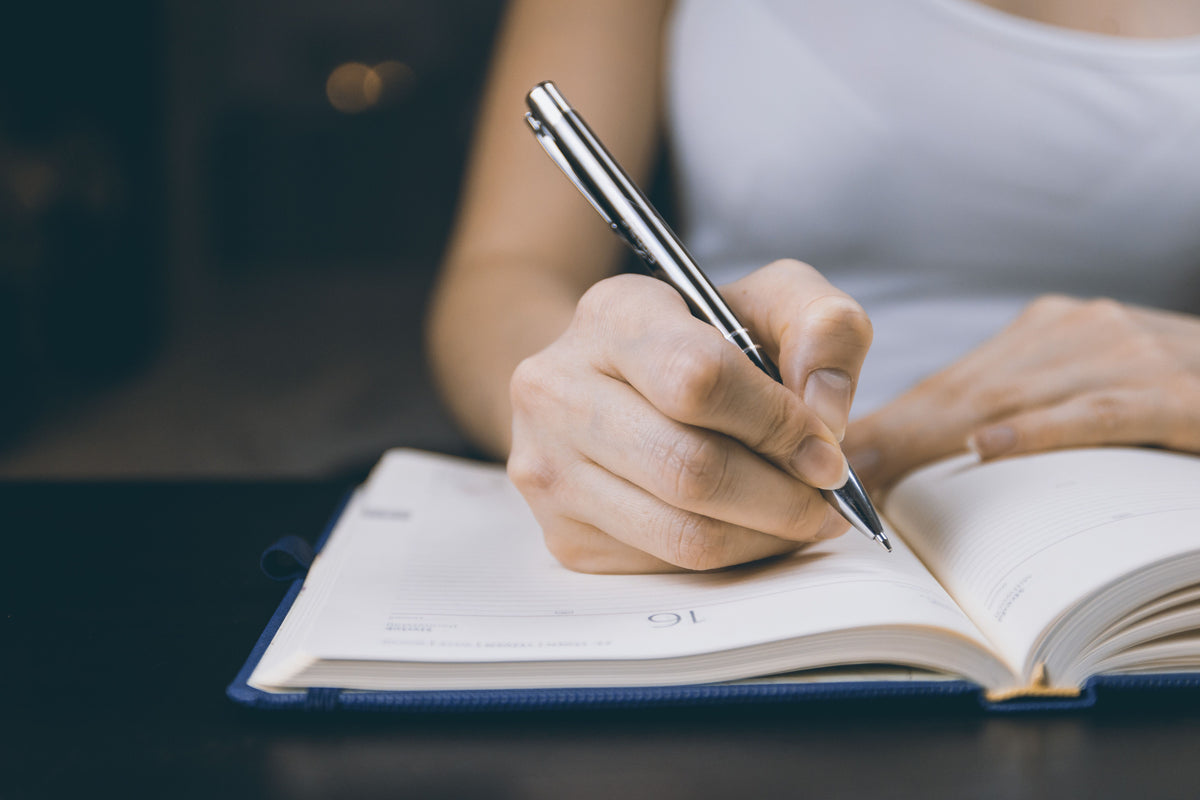 A writer drafting longhand in a notebook with a ballpoint pen.