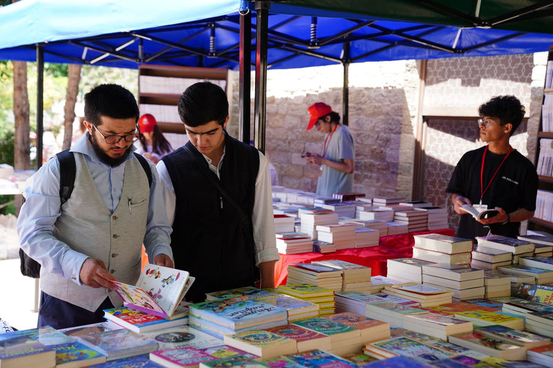 Visitors browsing tables piled with books at a sunny outdoor book fair