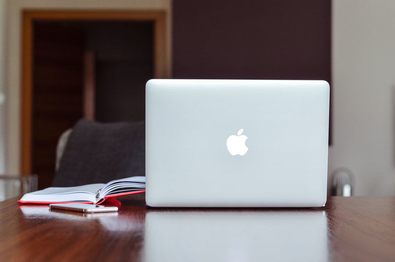 Laptop beside an open book on a bright wooden desk, ready for self-publishing