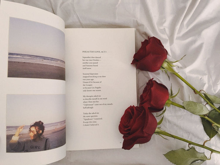 Open poetry book resting beside fresh roses on a white sheet